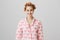 Treat yourself. Portrait of modern cute young woman in hair curlers and pyjamas, standing with facial cream on cheeks