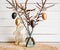 Tree branches in vase with black and bronze colored Easter eggs hanging on string, white rustic wood board background.