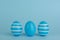 Tree Easter decorated blue eggs in a row. Blue background. Copy space.