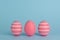 Tree Easter decorated pink eggs in a row. Blue background. Copy space.