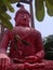 Tree leaves obscure the huge cement plaster red statue of sitting Buddha, which stands 18 feet tall.