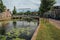 Tree-lined canal with aquatic plants, brick houses and bridge in a sunny day in Weesp.