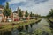 Tree-lined canal with aquatic plants, brick houses and trees in a sunny day in Weesp.