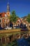Tree-lined canal with boat, church bell tower and brick houses at the bank on sunset in Weesp.
