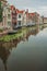 Tree-lined long canal with aquatic greenish plants, brick houses on its bank and cloudy day at Gouda.