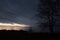 Tree silhouette in the foreground with a beautiful, overcast and moody sunset sky in the background, over a lake