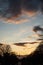 Tree silhouettes and suspended bridge solhouette under the river and beautiful cloudy sky by sunset