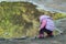Tree years old girl looking for pebbles on big summer puddle bank
