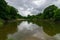 Trees and cloudy sky reflecting in calm section of a river