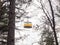 Among the trees you can see a yellow retro cable car cabin against a cloudy sky