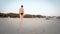 Trekking a fashion female model in bikini walk on empty beach sand at sunrise