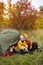 Trekking and hiking concept - happy couple in love sitting near green tent in autumn forest