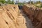 Trench for installation of water pipes.The reinforced concrete wall is covered with waterproofing mastic.Plastic pipes lie next to