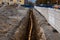 Trench with orange plastic pipe laid in it at construction site