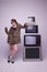 In trends. Young girl in stylish animal print coat and trendy sunglasses posing near retro TV sets against grey studio