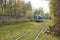 Trendy blue tram rides along the rails in the Park or green part of the city. Green foliage, modern city ecological transport tram