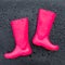 Trendy bright pink rubber boots on black wet surface covered with raindrops.