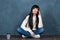 Trendy brunette girl sits on the floor, talks on the phone and smiles. Studio portrait on a monochrome blue, trendy shabby