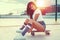 trendy brunette woman sitting on skateboard in sunset