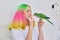 Trendy with colored hair teenager girl with green parrot on hand