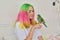 Trendy with colored hair teenager girl with green parrot on hand