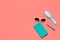 Trendy colorful flat lay composition. Coral colored desk with turquoise diary, hair comb, white glasses and pen