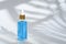 Trendy dropper glass bottle with pipette and blue liquid on white background with leaf shadow