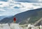 Trendy guy in a red jacket stands on a marble rock and looking toward the summer valley. Sport adventure and active life