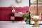 Trendy living room interior with wicker peacock chair and handmade pastel pink and burgundy chest of drawers