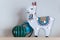 A trendy llama kids night lamp standing on a bedside table in dawn or sunrise light with ceramic cactus and a plastic globe.