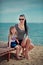 Trendy mother with black hairs and red lips in sun glasses enjoy summer time on a beach with her baby daughter ,Adorable scene of