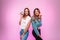 Trendy positive women with smiles in trendy casual jeans clothes with sweet donuts posing near a vintage pink wall in the studio.