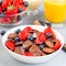 Trendy small chocolate cereal pancakes with condensed milk, strawberry, blueberry and orange juice, in a white bowl, square