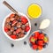 Trendy small chocolate cereal pancakes with condensed milk, strawberry, blueberry and orange juice, in a white bowl, square format