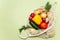 Trendy string bag with fresh vegetables and greens over light green background: potatoes, tomatoes, onion, bell pepper