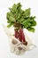 Trendy string bag with fresh young beetroot and haulm over light white background