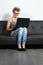 Trendy teenager girl sitting on a couch with a laptop and glasses