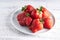 Trendy ugly strawberries in a plate on a light background