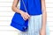 Trendy woman in blue blouse and white lace skirt holding small blue leather bag w