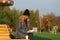 Trendy woman in stylish coat sitting on the bench in city park. Urban scene outdoors.