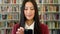 Trendy woman using her phone in a library to research. Young, stylish student browsing an online ebook reader app or