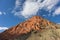 Triangle mountain formed by orange and red rock. Green vegetation, cloudy sky. Picture taken during dry season. Simpons gap, West