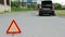 Triangle warning sign on road foreground and car with blinker lights on road wayside