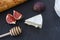 Triangular appetizing piece of camembert cheese, pieces of figs in honey and a wooden spoon for honey and baguette on a graphite b