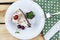 A triangular piece of tiramisu on a white plate, a piece of chocolate, a cherry