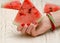 Triangular piece of watermelon in a female hand with a manicure on a light wooden background