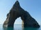 A triangular rock with an arch in the middle protrudes from the sea