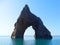 A triangular rock with an arch in the middle protrudes from the sea