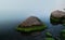 A triangular stone near the shore of a reservoir during fog. Nicely overgrown with green algae at the base.