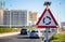 A triangular warning sign with flashing lights stands in front of a roundabout.
